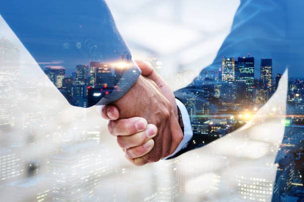 A business handshake over a night-time city skyline